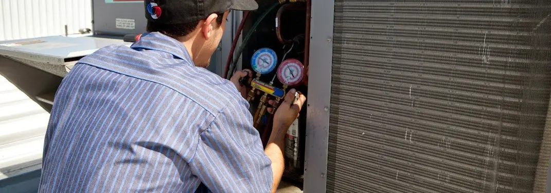 HVAC technician servicing a condenser unit in Roy